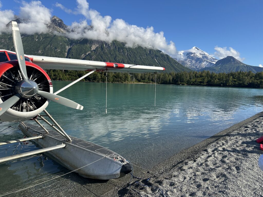 Floatplane float and propeller on a sandy beach below snow-capped mountains